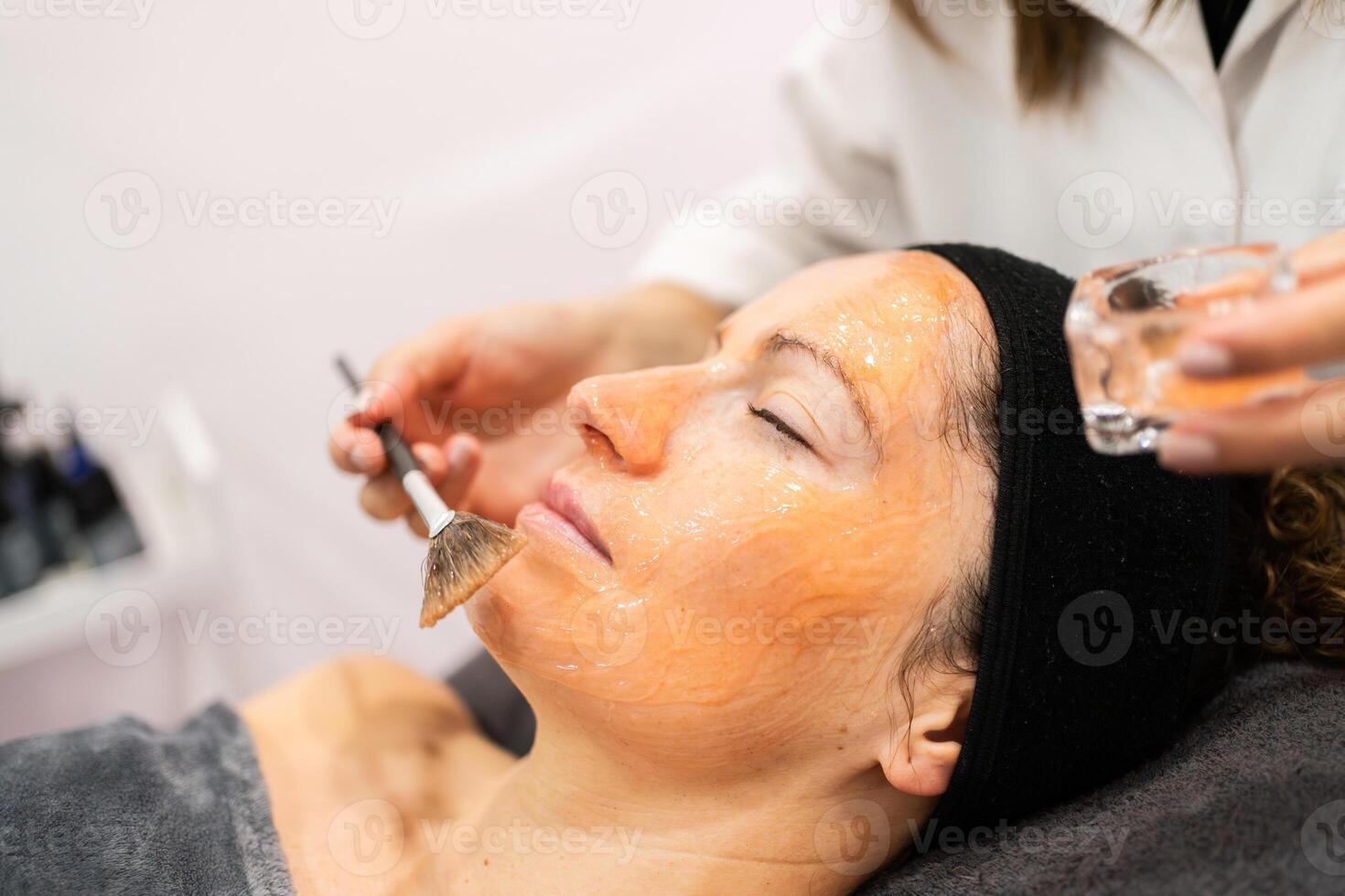 cosecha cosmetólogo aplicando gel en hembra cara con cepillo en belleza salón foto