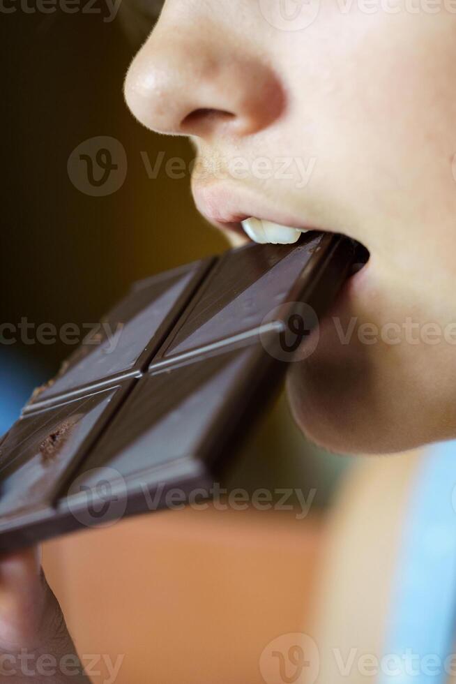 Anonymous girl biting yummy chocolate bar at home photo