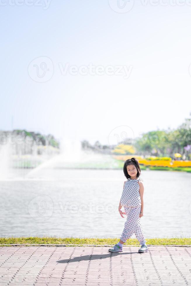 Girl in Polka Dots Walking by Sunny Waterfront, Kid takes graceful walk along the waterfront, with the bright sunshine enhancing the joyful atmosphere of lively park. Vertical image.Child age 6 years. photo