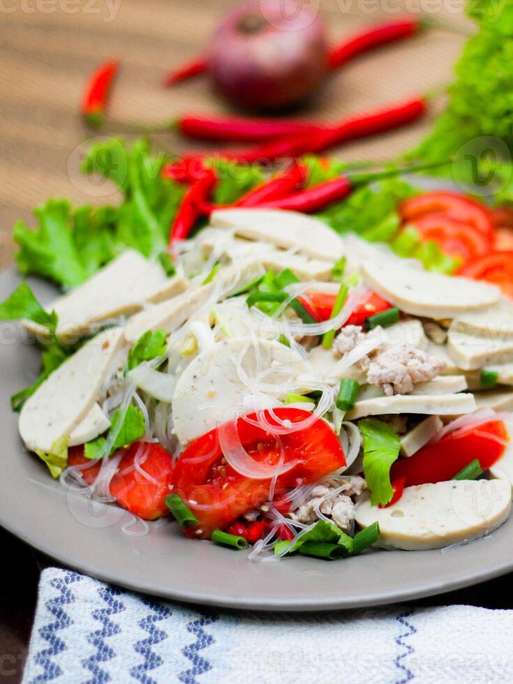 Spicy Glass Noodle Salad with Vietnamese Sausage  served in a gray plate Put on a wooden table and various vegetables. photo