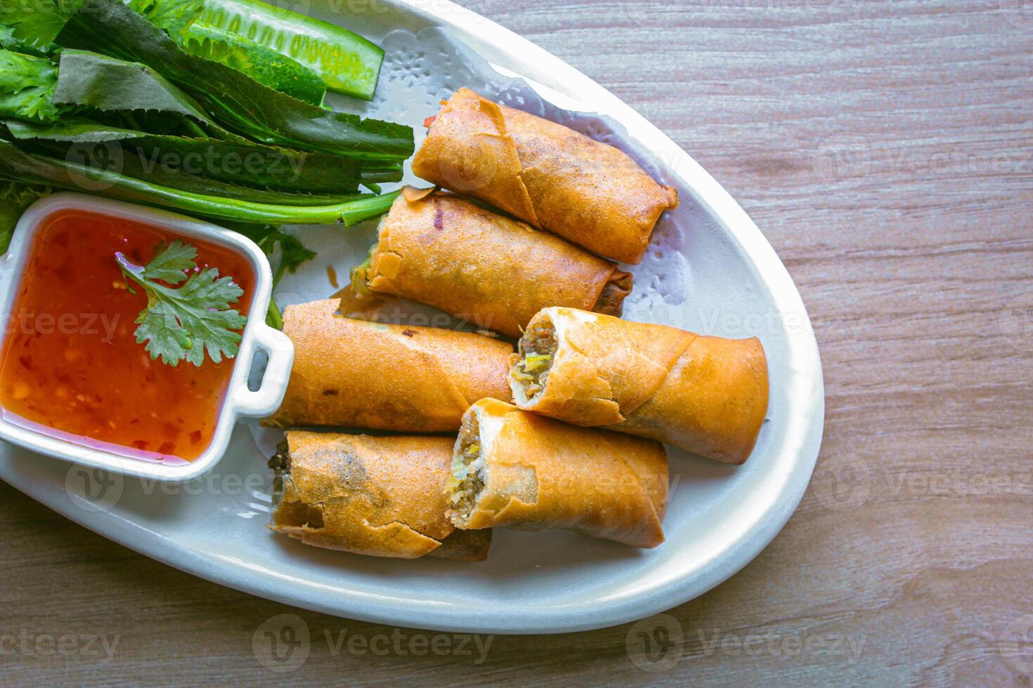 Freshly fried golden yellow spring rolls on a white plate with various vegetables and a delicious dipping sauce, top view. photo