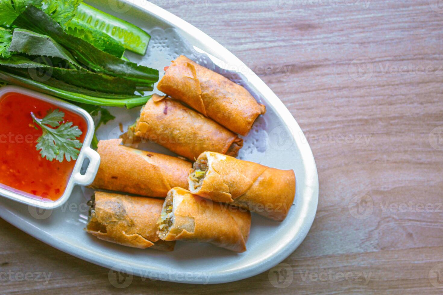 Freshly fried golden yellow spring rolls on a white plate with various vegetables and a delicious dipping sauce, top view. photo