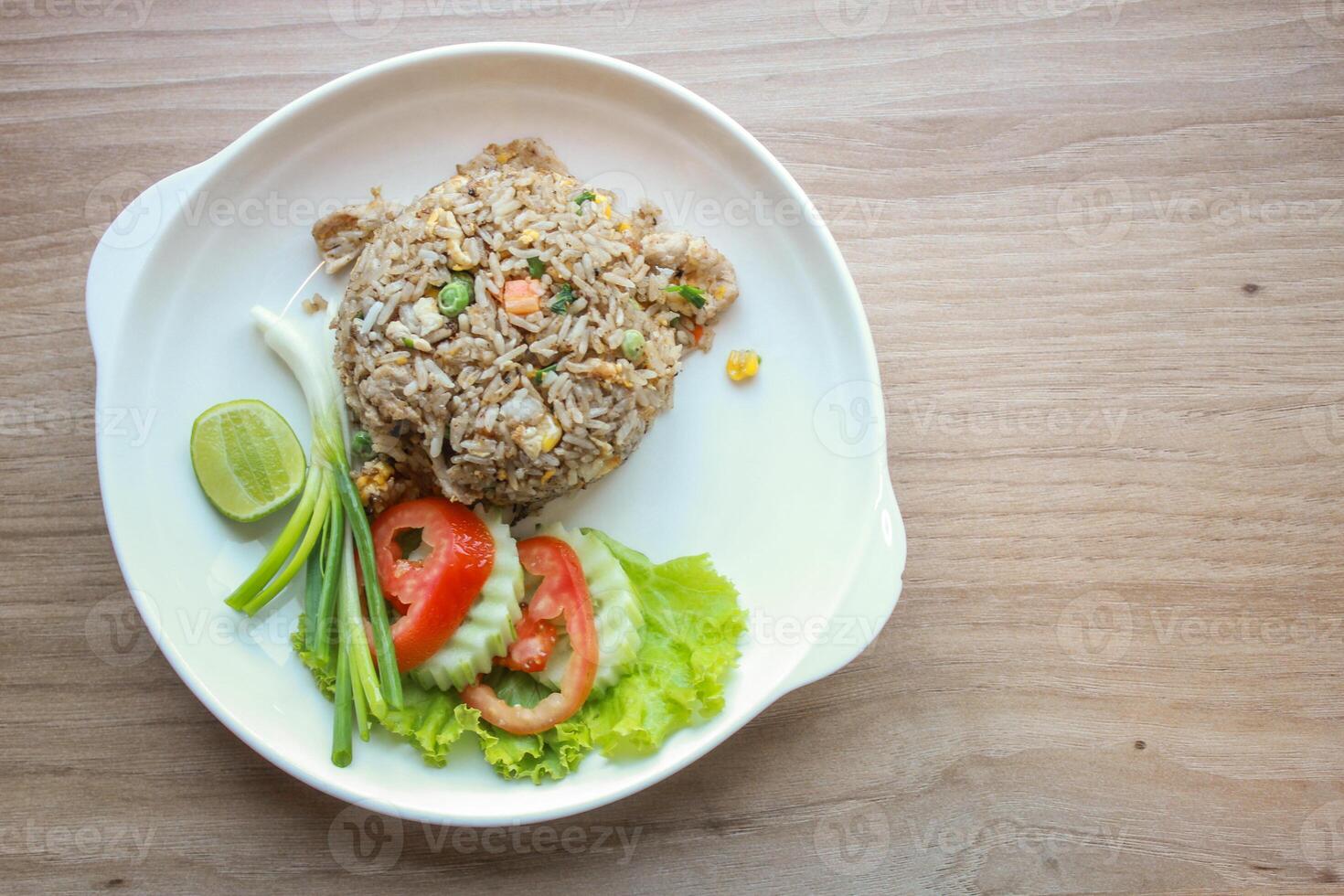 Pork fried rice served in a restaurant with wooden floor tables with tomatoes, cucumbers, scallions, fried rice, delicious food made from steamed rice, top view photo