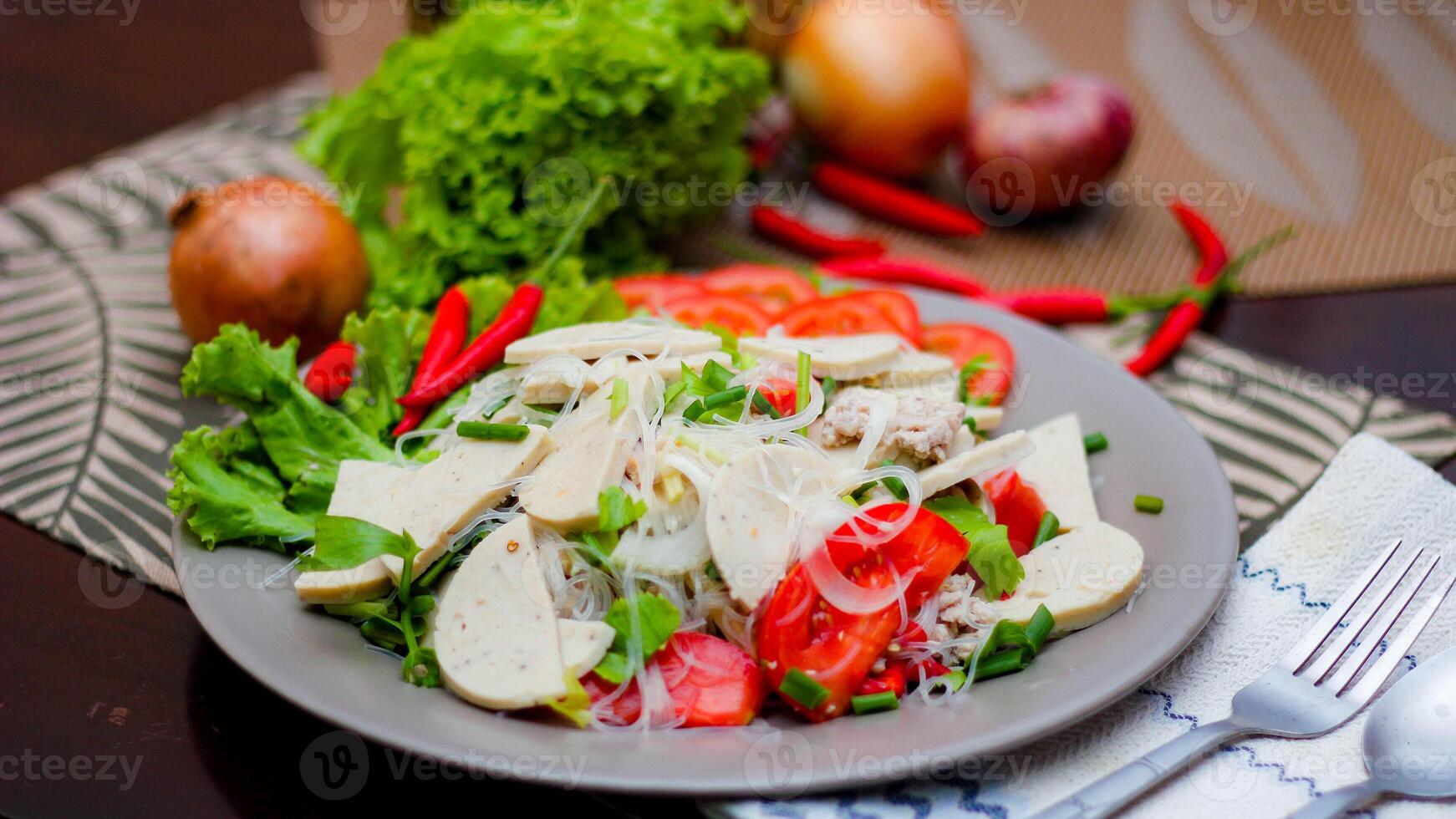 Spicy Glass Noodle Salad with Vietnamese Sausage  served in a gray plate Put on a wooden table and various vegetables. photo