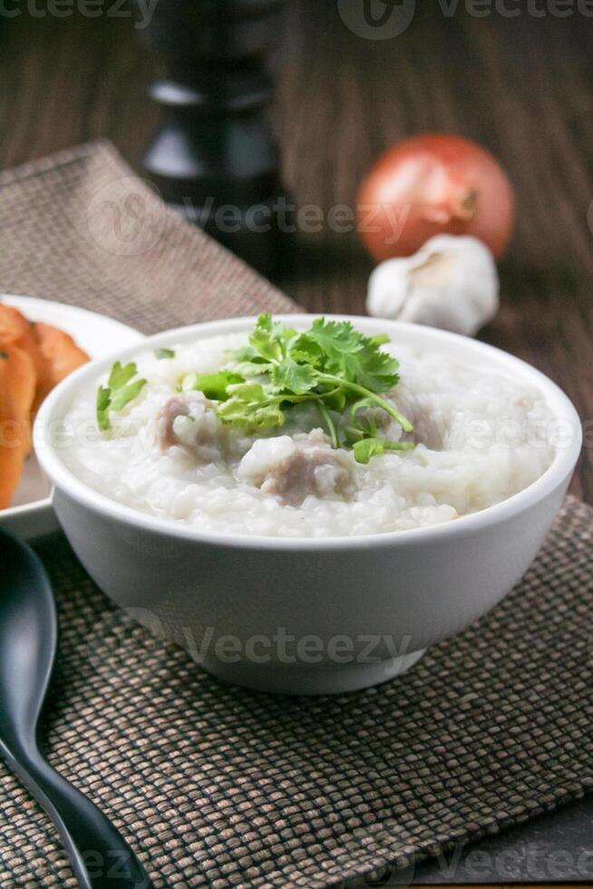 Pork porridge with coriander and ginger or porridge is similar to rice porridge but softer in texture. Served on a wooden table with patongko. For breakfast in the morning or evening photo