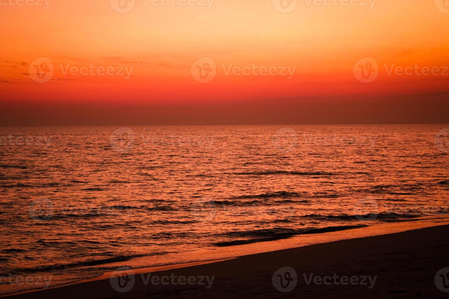 The sea after sunset has an orange glow and an orange sky with no clouds. photo
