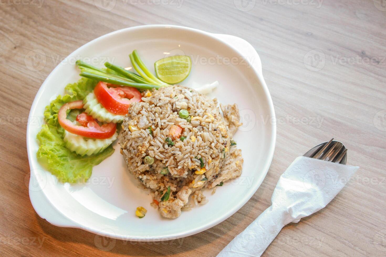 Pork fried rice served in a restaurant with wooden floor tables with tomatoes, cucumbers, scallions, fried rice, delicious food made from steamed rice. photo