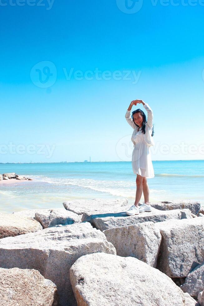 Beautiful woman in white dress standing on the beach and looking at the sea photo