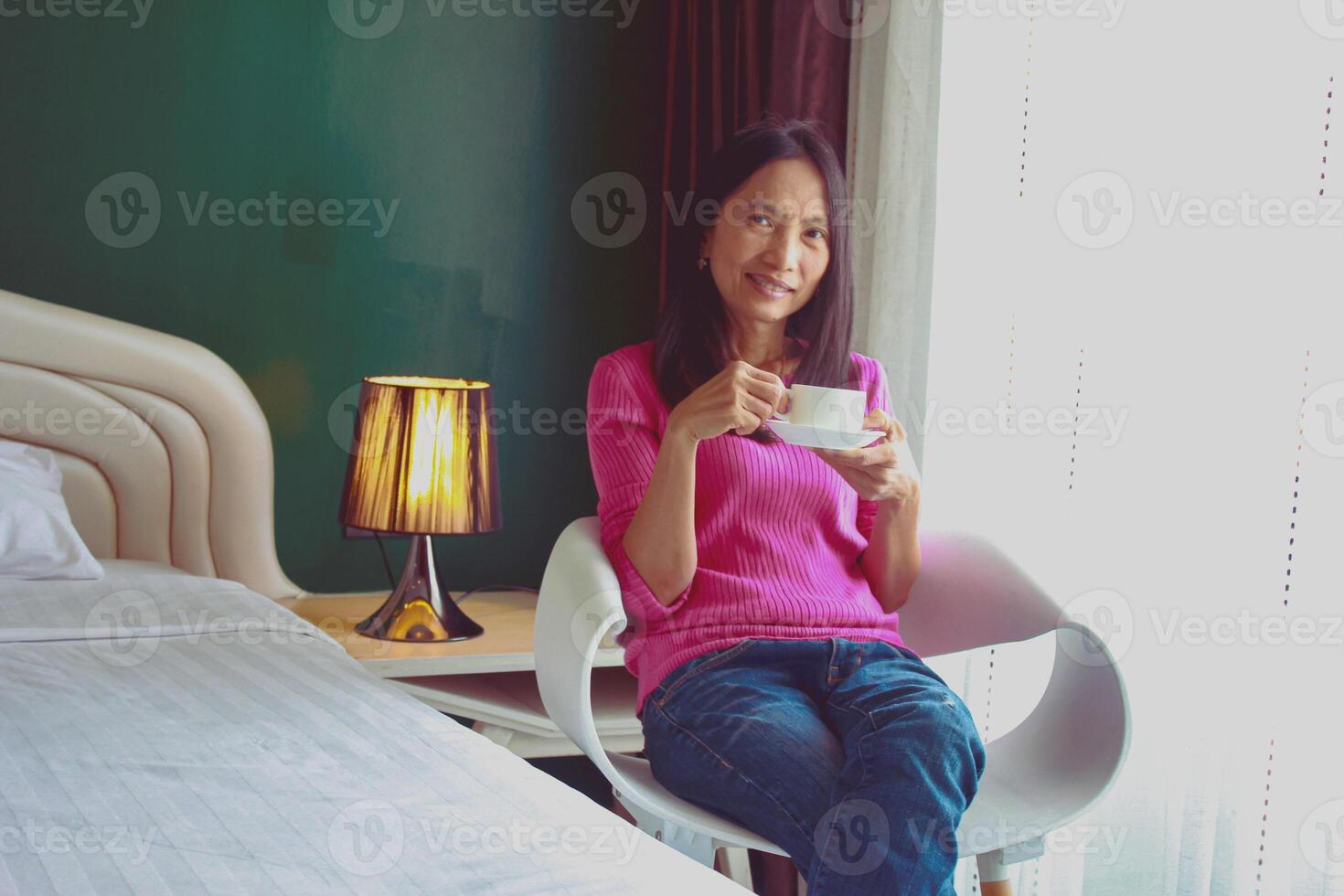 Portrait of beautiful young Asian woman holding cup of morning coffee in white bedroom, happy, cheerful, relaxing in summer. Thai Asian makeup ideas, white bedroom photo