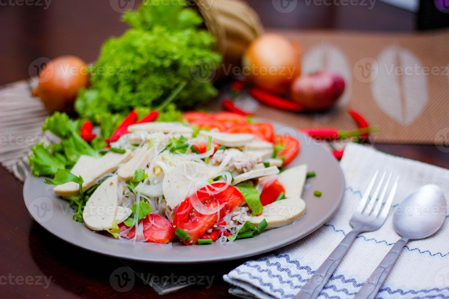 Spicy Glass Noodle Salad with Vietnamese Sausage  served in a gray plate Put on a wooden table and various vegetables. photo