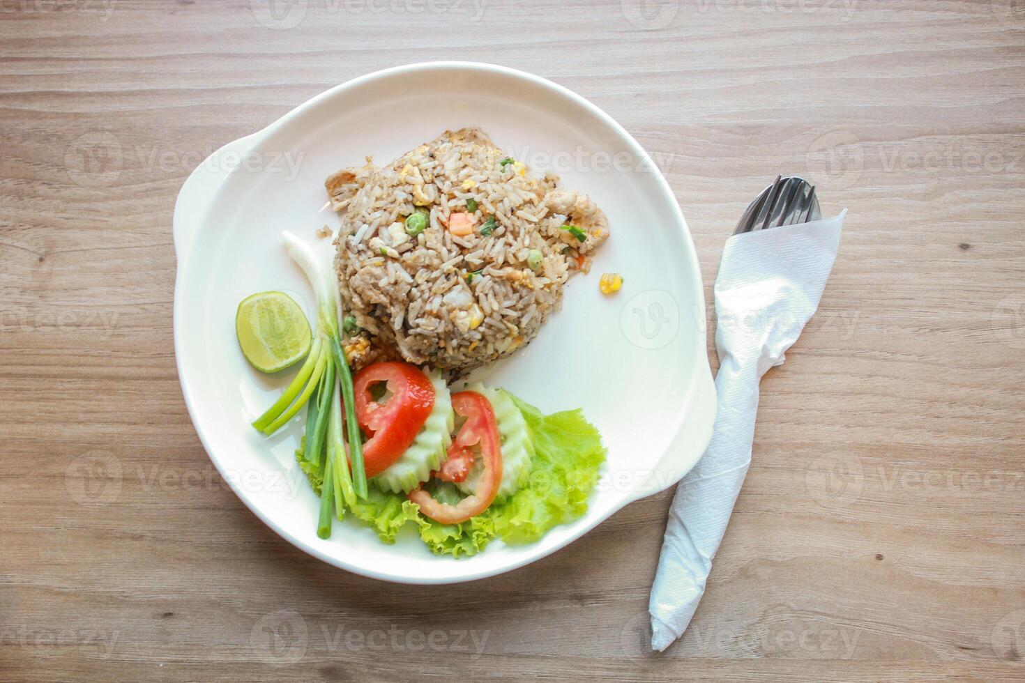 Pork fried rice served in a restaurant with wooden floor tables with tomatoes, cucumbers, scallions, fried rice, delicious food made from steamed rice, top view photo