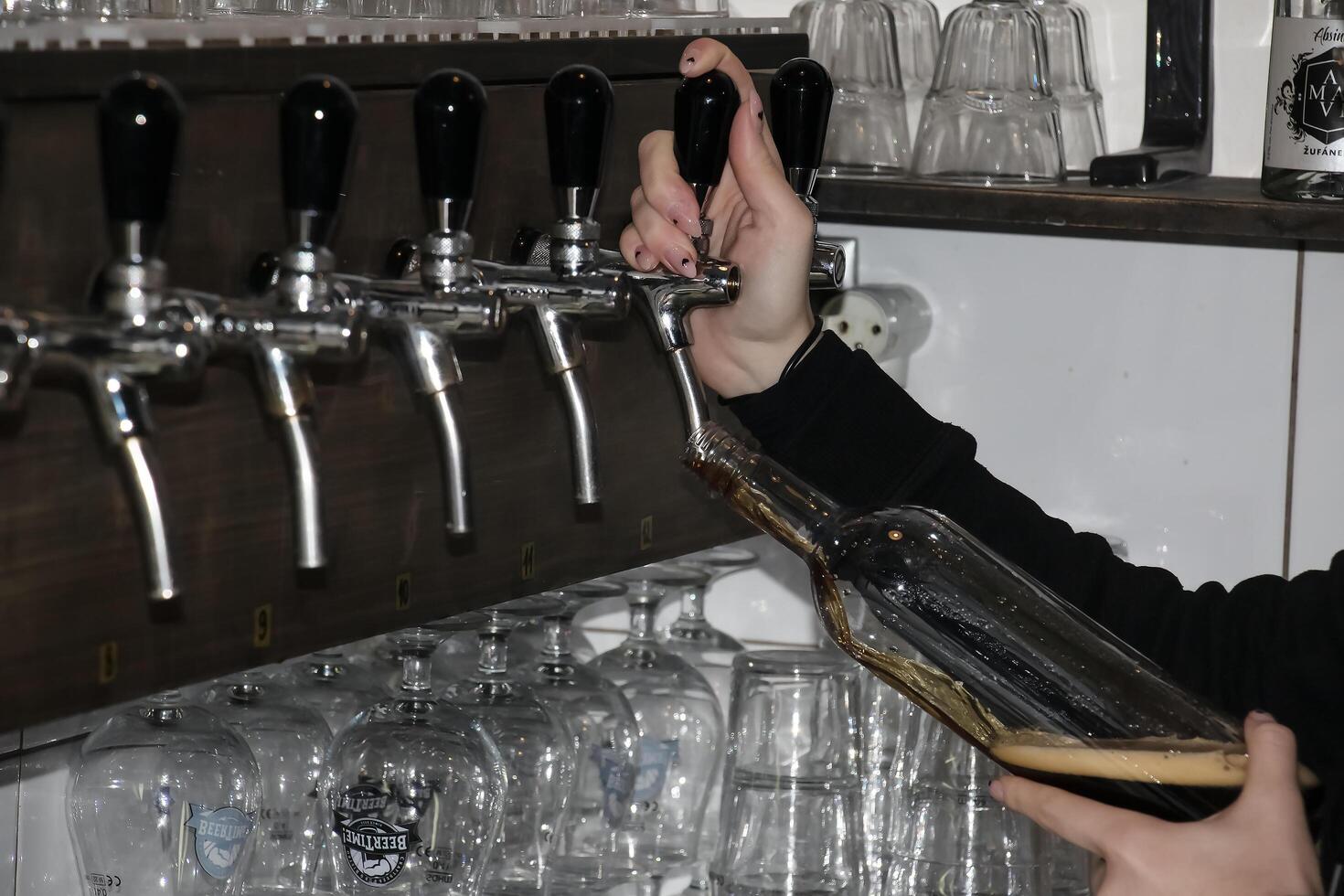 detrás el encimera. De las mujeres manos hermosamente y fácilmente verter cerveza dentro un botella. foto