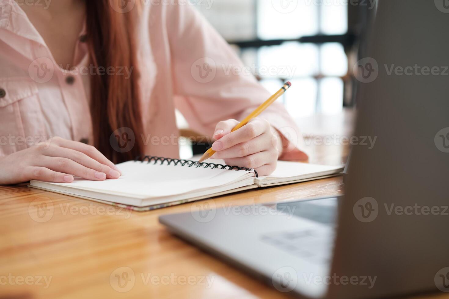 Close-up of a student's hand writing notes in a notebook while engaged in online learning, with a laptop visible. photo
