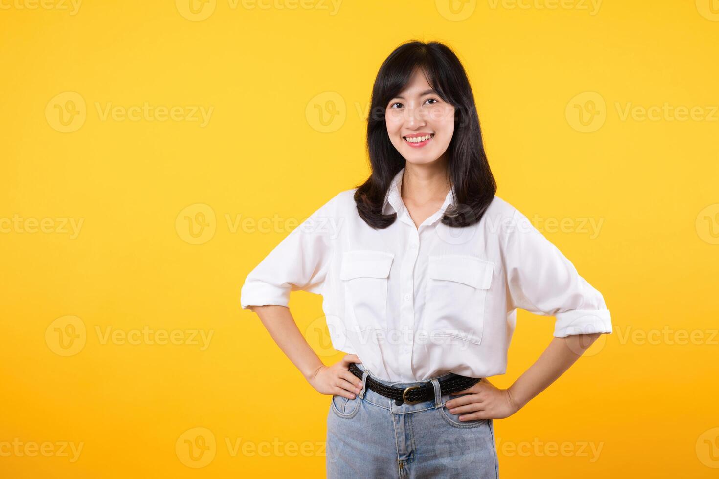 Portrait smiling young asian woman with arms akimbo Happy asia girl posing with arms on hips and looking at camera over yellow background and copy space Confident female get happy and feel relax. photo