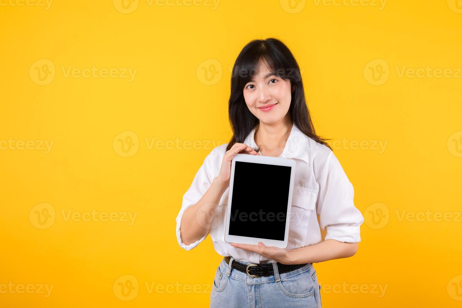 Confident asian woman embraces the digital age, holding tablet on a vibrant yellow background. modern connectivity, tech-savviness, and empowerment. digital lifestyles and technological advancements. photo