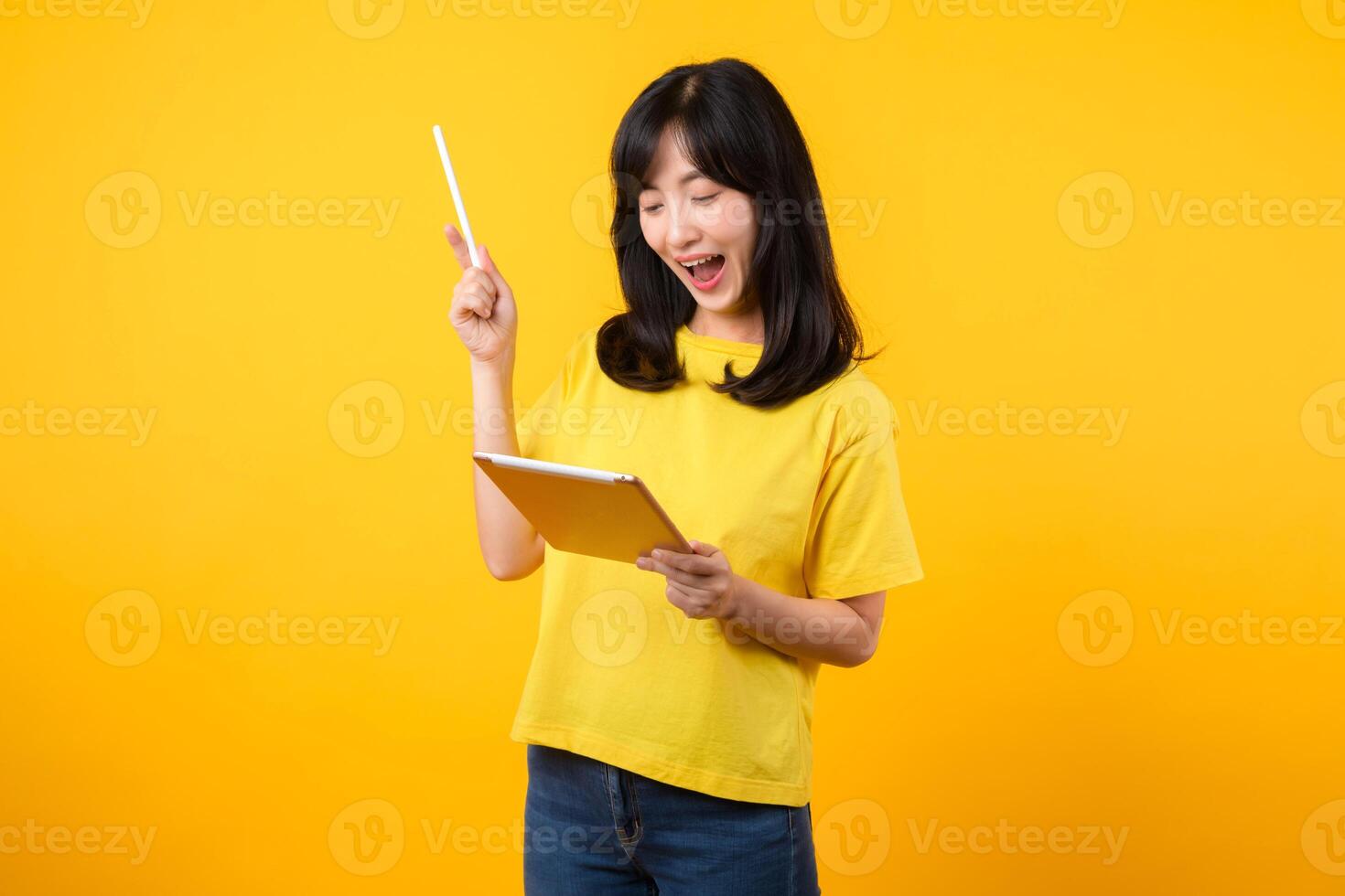 young Asian woman wearing yellow t-shirt and jeans showing happy smile while using digital tablet, displaying thoughtful expression and creative idea. education technology innovative thinking concept. photo