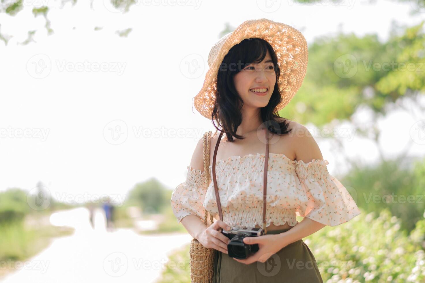 Portrait of asian young woman traveler with weaving hat and basket and a camera on green public park nature background. Journey trip lifestyle, world travel explorer or Asia summer tourism concept. photo