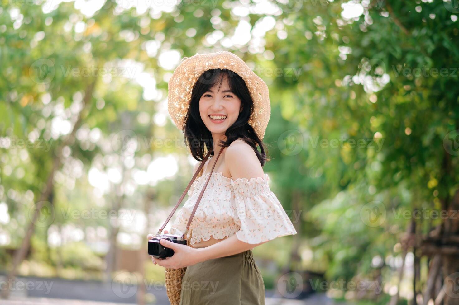 Portrait of asian young woman traveler with weaving hat and basket and a camera on green public park nature background. Journey trip lifestyle, world travel explorer or Asia summer tourism concept. photo