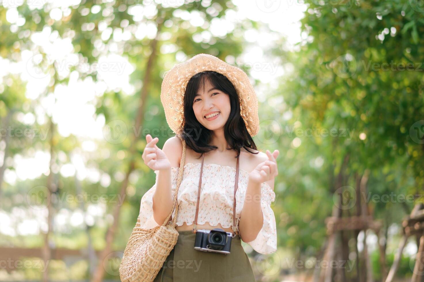 Portrait of asian young woman traveler with weaving hat and basket and a camera on green public park nature background. Journey trip lifestyle, world travel explorer or Asia summer tourism concept. photo