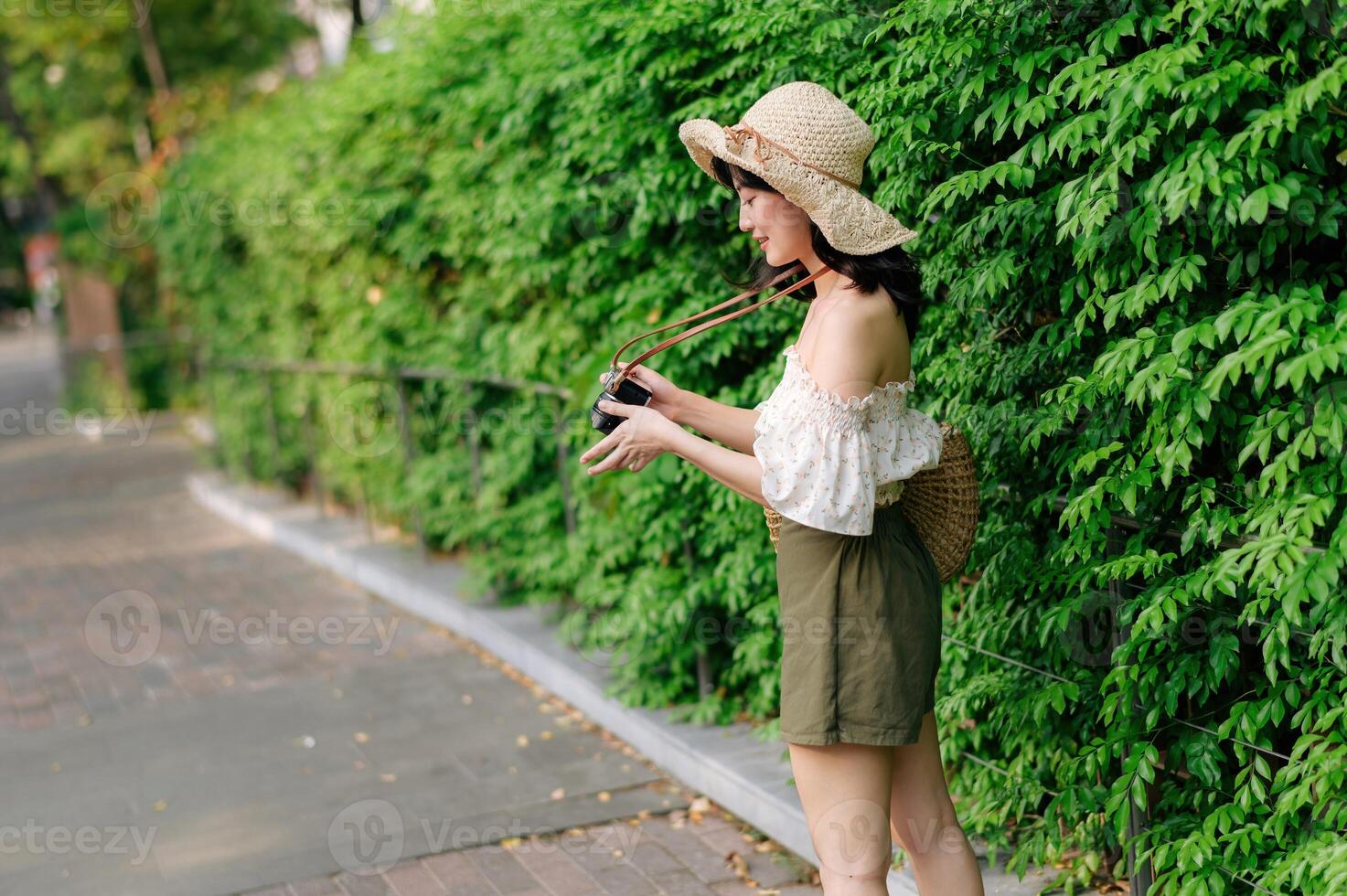 Portrait of asian young woman traveler with weaving hat and basket and a camera on green public park nature background. Journey trip lifestyle, world travel explorer or Asia summer tourism concept. photo