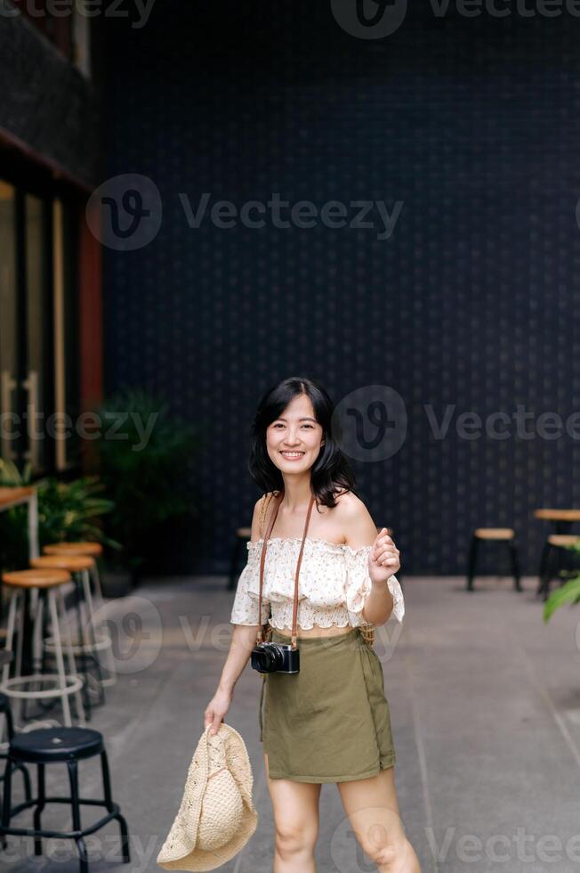 Happy youth asian woman with camera travels street city trip on leisure weekend. Young hipster female tourist sightseeing summer urban Bangkok destination. Asia summer tourism concept. photo