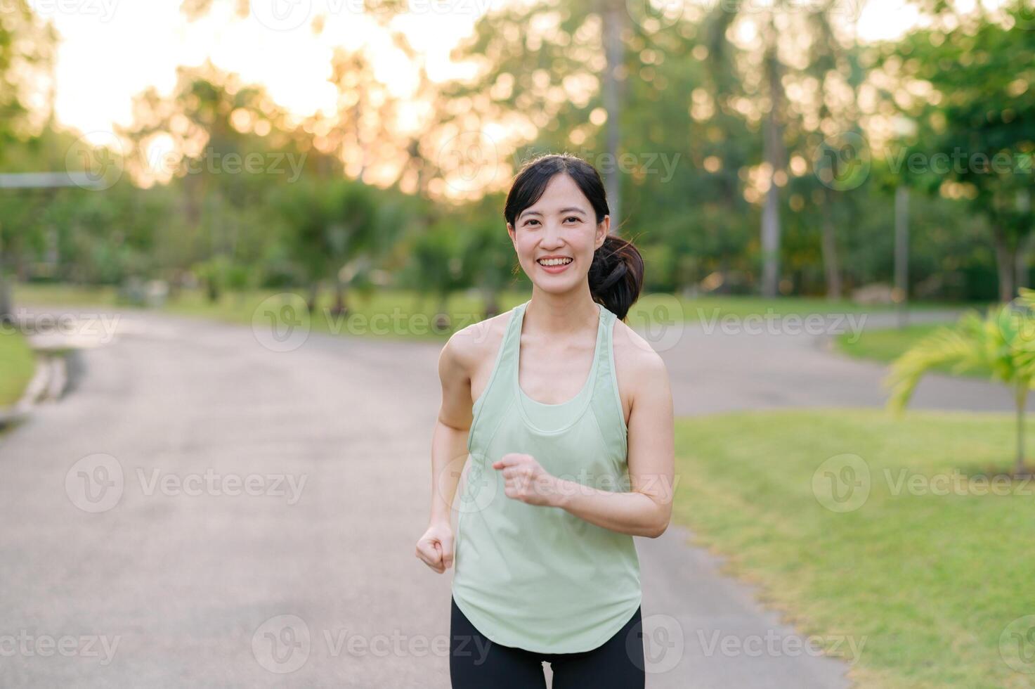 Fit Asian young woman jogging in park smiling happy running and enjoying a healthy outdoor lifestyle. Female jogger. Fitness runner girl in public park. healthy lifestyle and wellness being concept photo