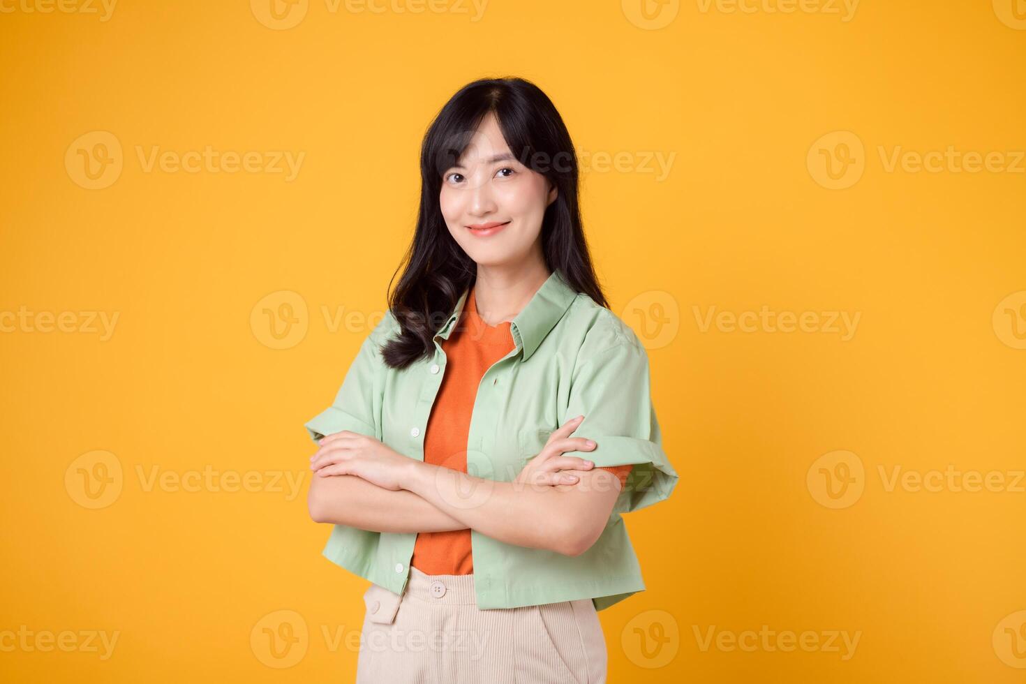 Radiate confidence portrait of Asian woman wears green shirt on orange shirt and show happy smile while confidently crossing her arms. Perfect for capturing sense of self assurance and empowerment. photo