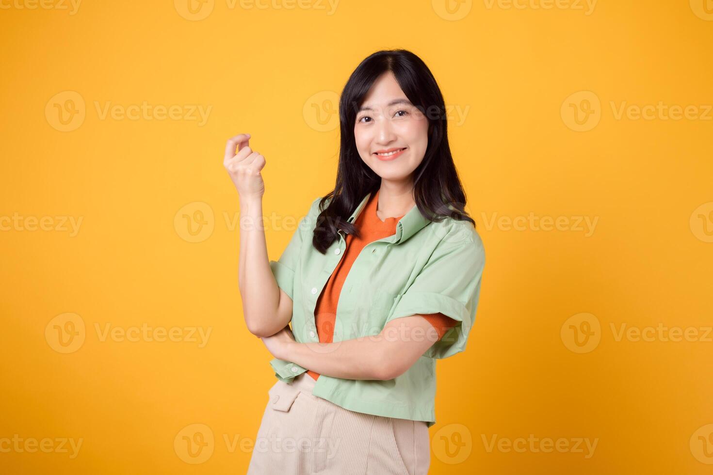 cheerful Asian woman 30s wearing green and orange shirt. With crossed arms, exudes self-assurance and poise. Perfect for capturing the essence of confidence and showcasing a vibrant fashion concept. photo