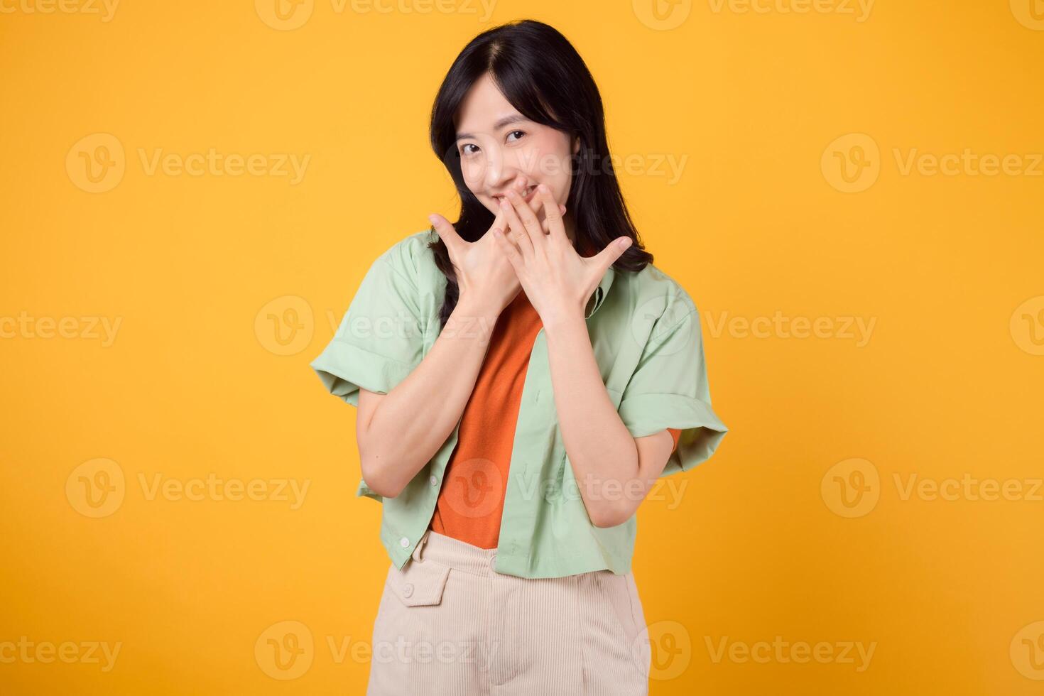 shy young asian woman 30s covering her mouth with hands isolated on yellow background. expression of embarrassment or uncertainty. shyness, embarrassment, and body language concept. photo