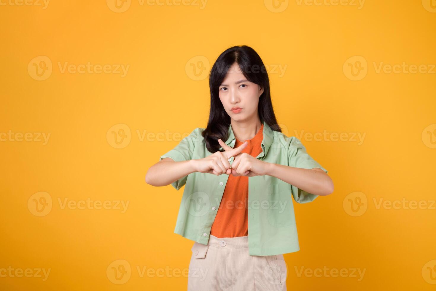 portrait young asian 30s woman expression serious negative face and showing cross finger deny hand gesture isolated on yellow background. wrong, no, stop and rejection body sign symbol concept photo