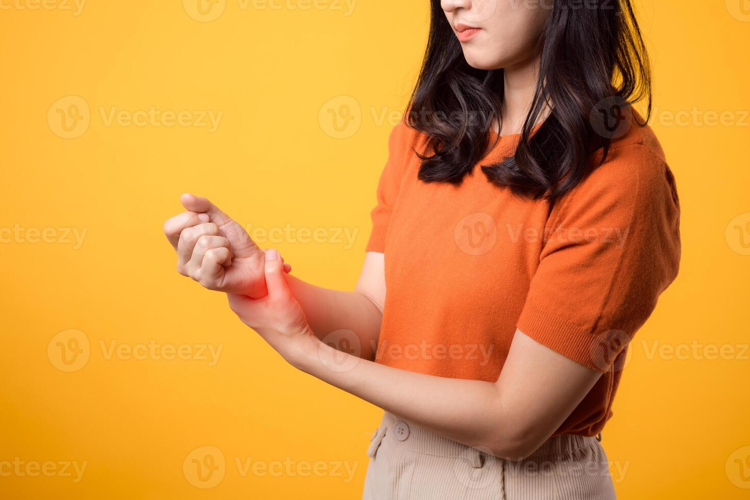 Young Asian woman in her 30s with wrist injury. holding her wrist and looking pained against yellow background. close-up perspective. wrist injuries, pain, inflammation, and medical care concept. photo