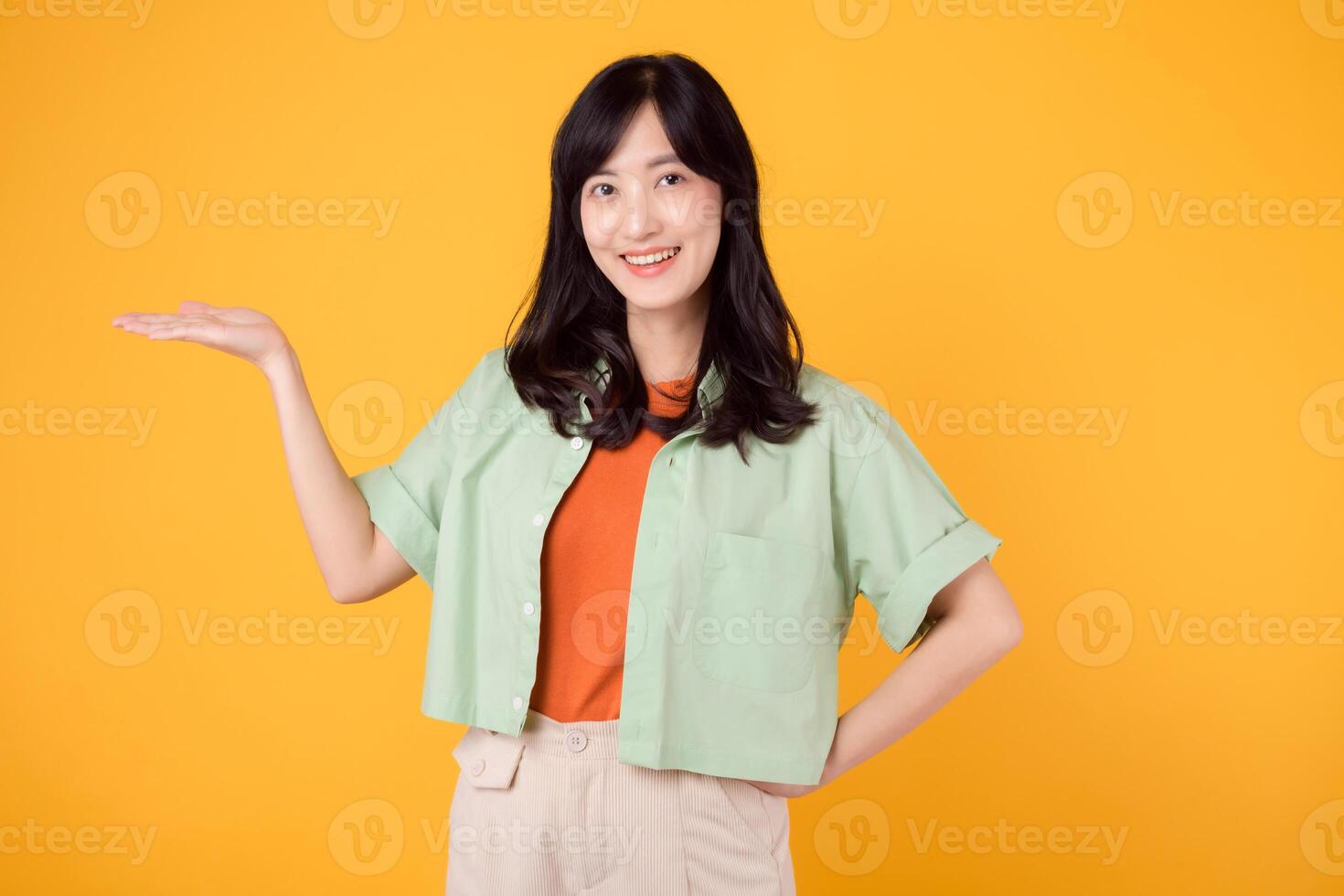 Vibrancy and joy portrait Asian young woman wears pastel green shirt on orange shirt and show happy smile while pointing hand gesture to free copy space. Perfect for adding lively touch to projects. photo