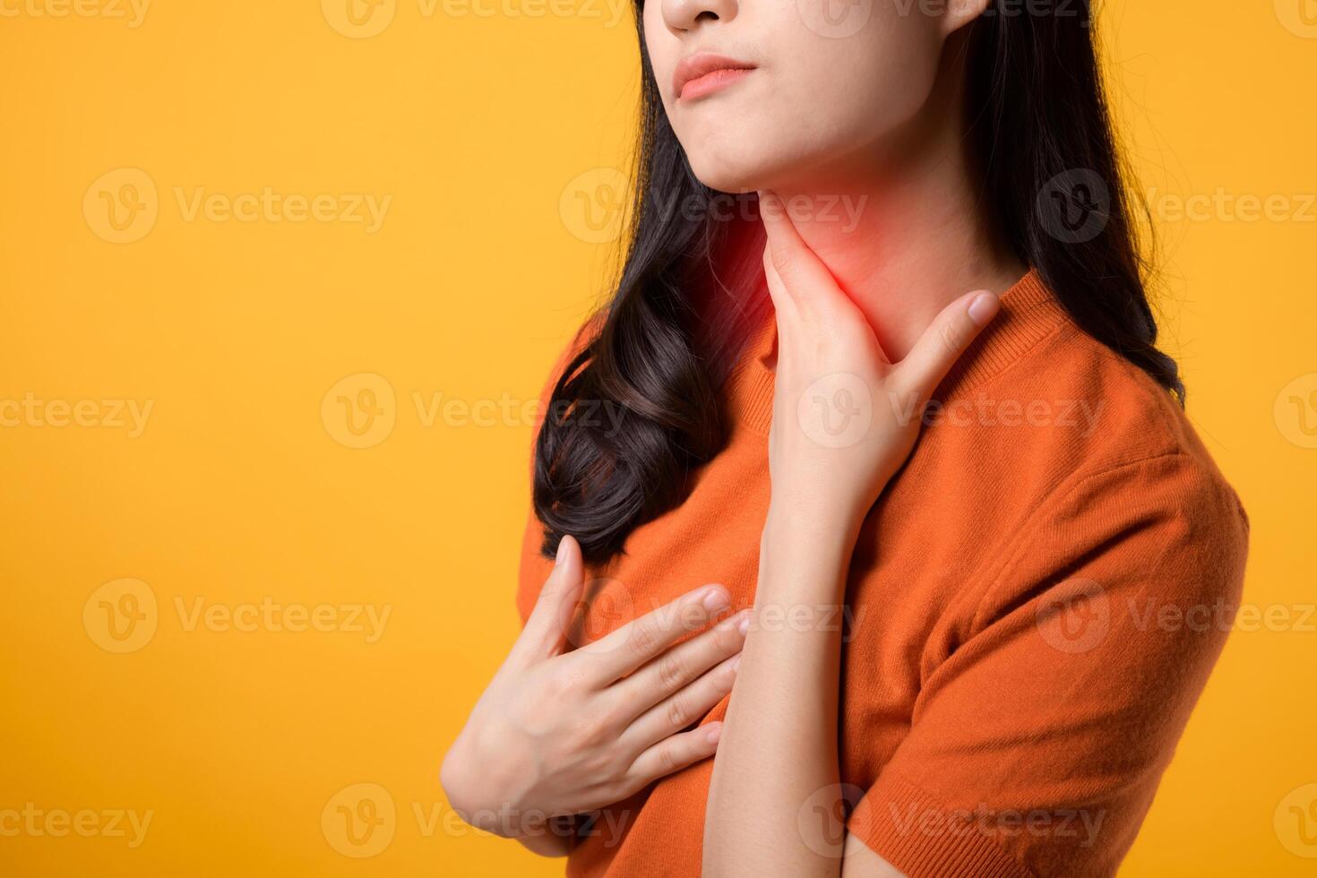 Expressing care wellness, cheerful young Asian woman in 30s wearing orange shirt holding her throat, portraying sore throat. Perfect for representing health concerns and the importance of self-care. photo