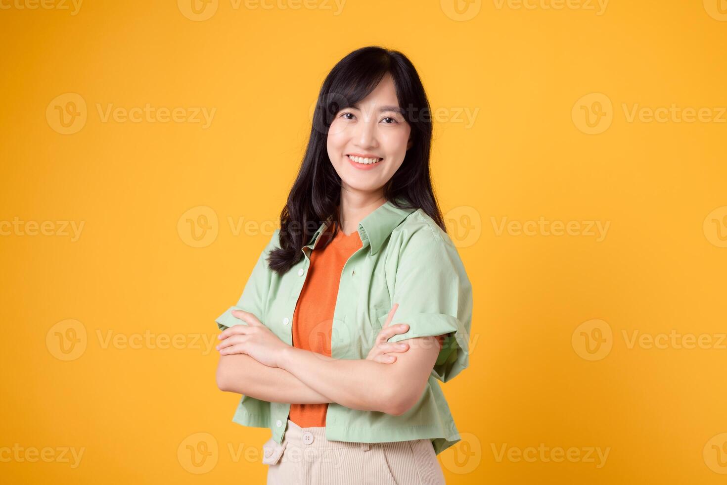 Radiate confidence portrait of Asian woman wears green shirt on orange shirt and show happy smile while confidently crossing her arms. Perfect for capturing sense of self assurance and empowerment. photo