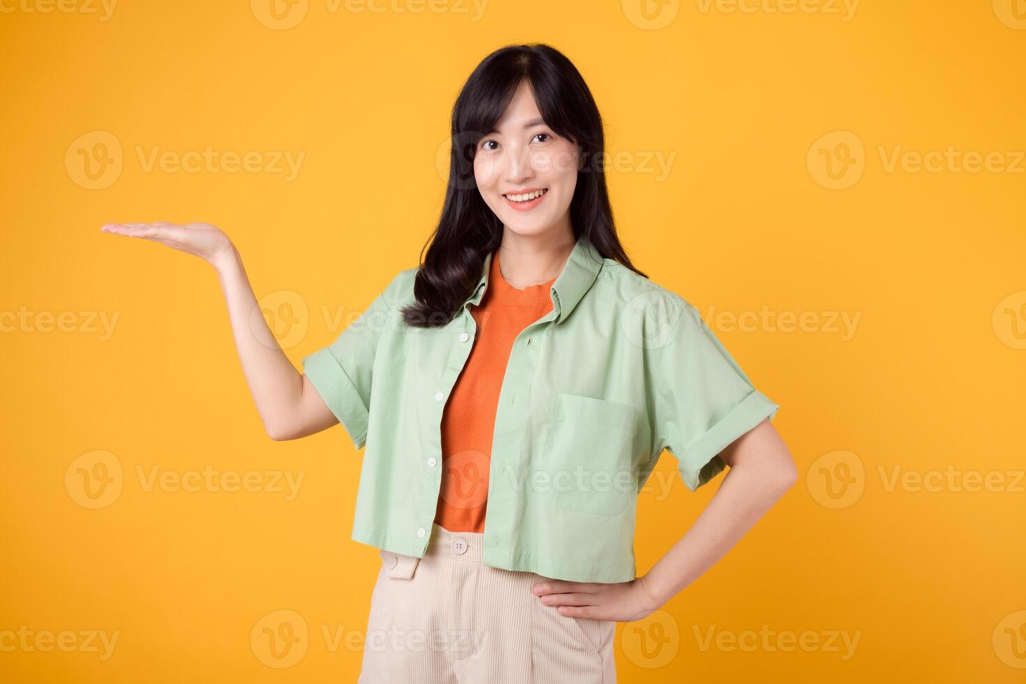 Vibrancy and joy portrait Asian young woman wears pastel green shirt on orange shirt and show happy smile while pointing hand gesture to free copy space. Perfect for adding lively touch to projects. photo