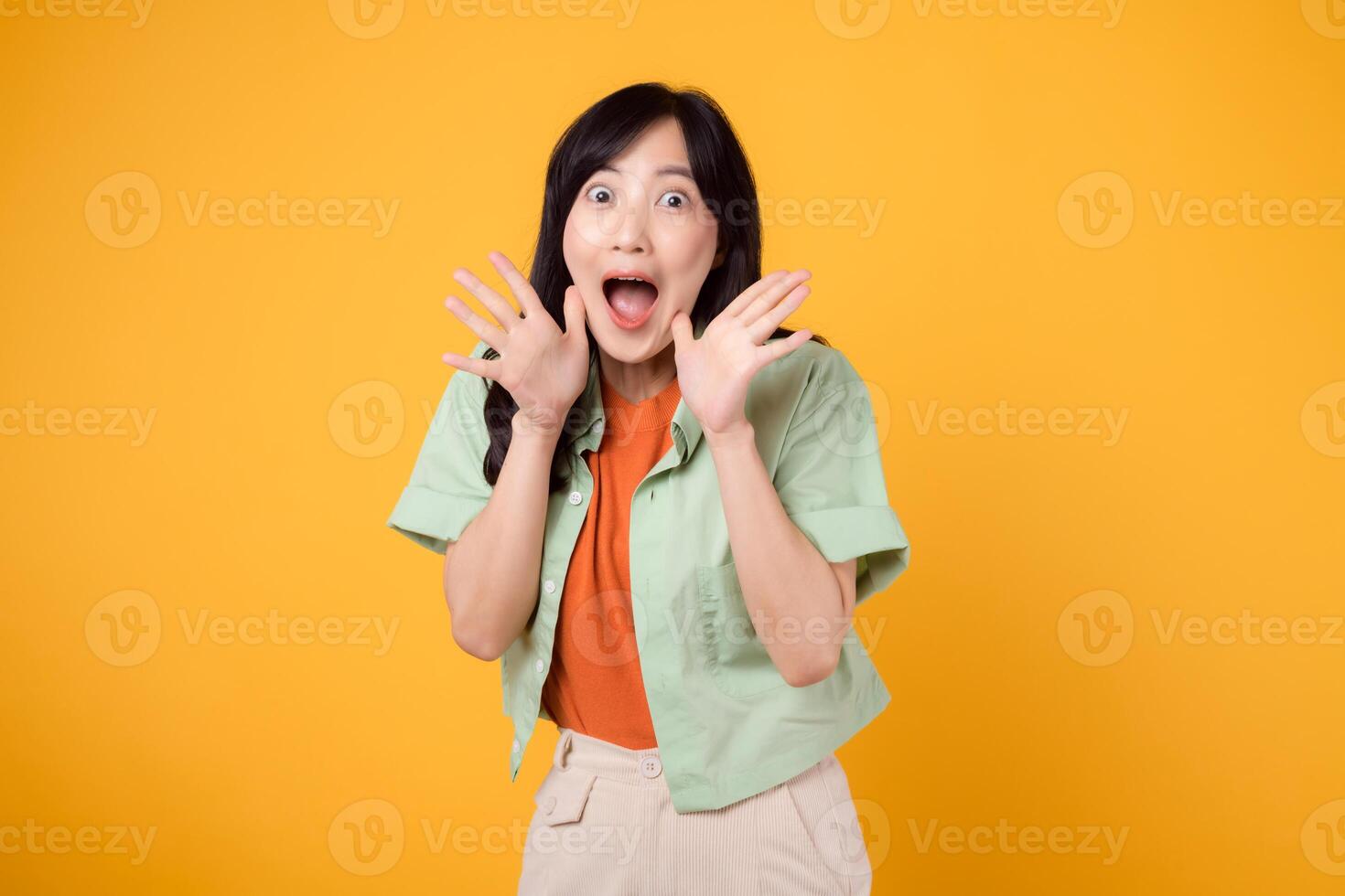 energético joven asiático mujer en su 30s vistiendo un verde y naranja camisa apasionadamente gritos con excitación. aislado en un amarillo fondo, representando el concepto de descuento compras promoción. foto
