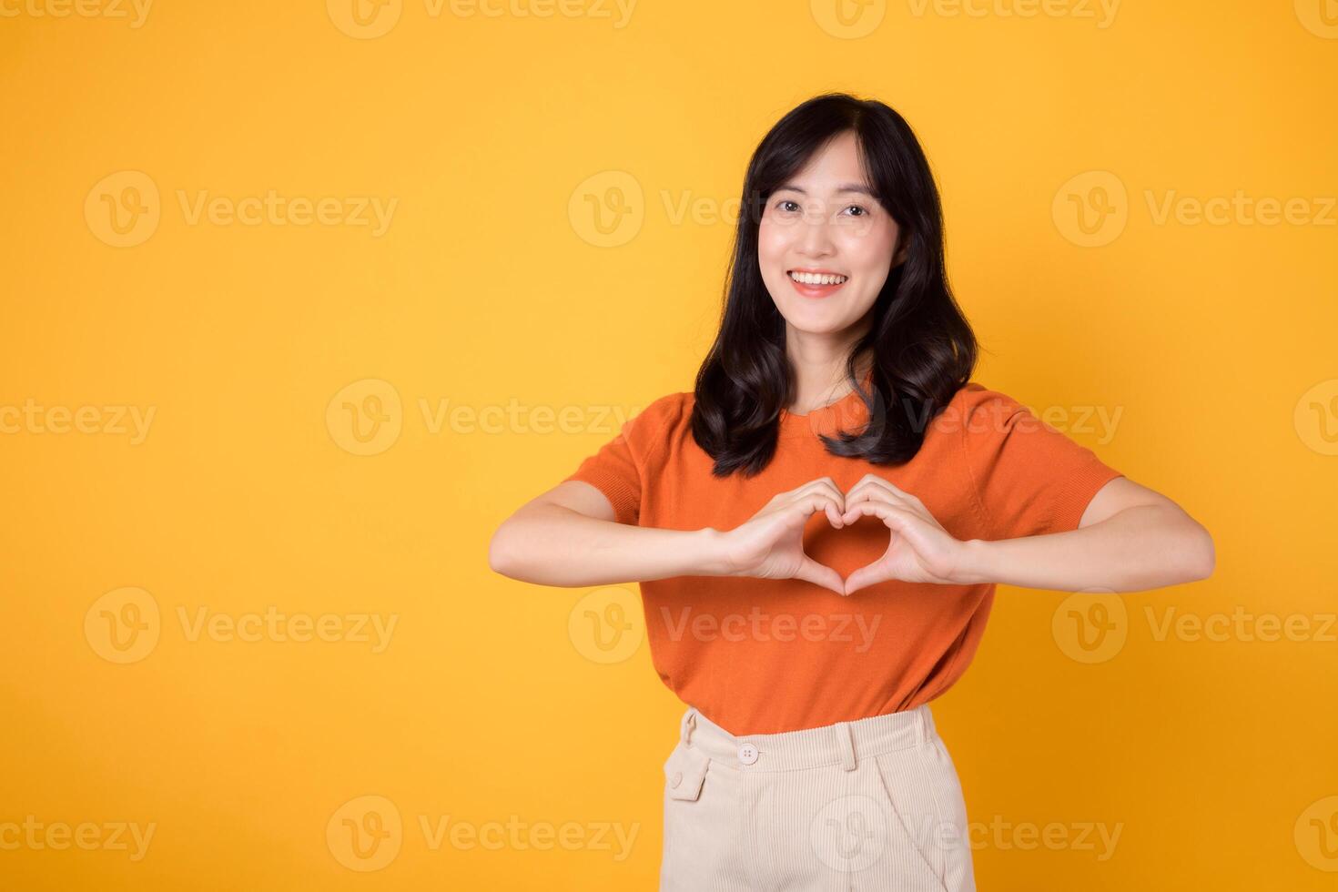 Embark on a journey of healthcare and wellness with an Asian woman in her 30s. Witness her heart hand gesture on a vibrant yellow background, symbolizing the embodiment of body wellness. photo