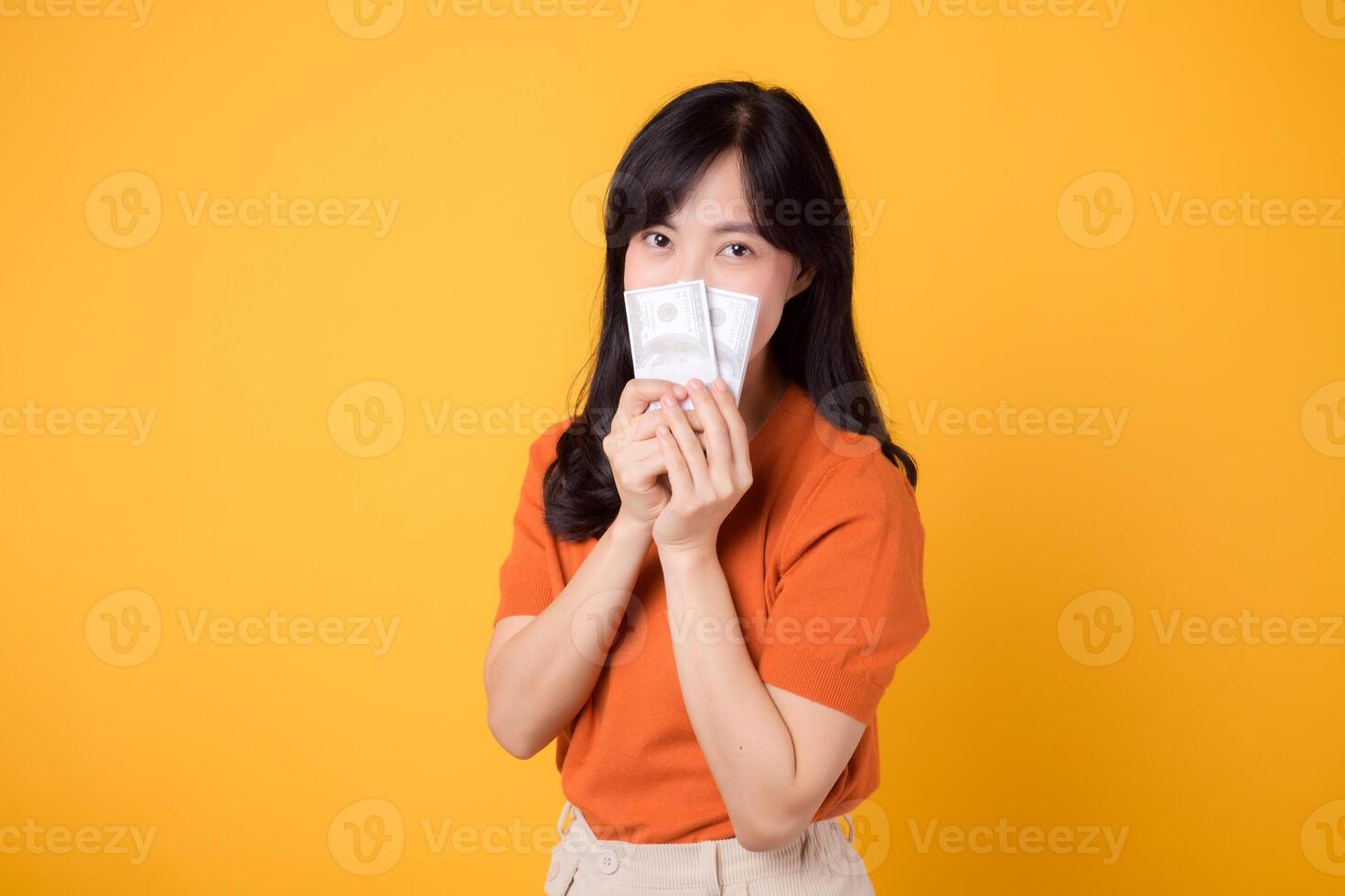 sonriente joven moderno 30s asiático mujer, participación efectivo dinero dólares, en pie terminado amarillo antecedentes foto