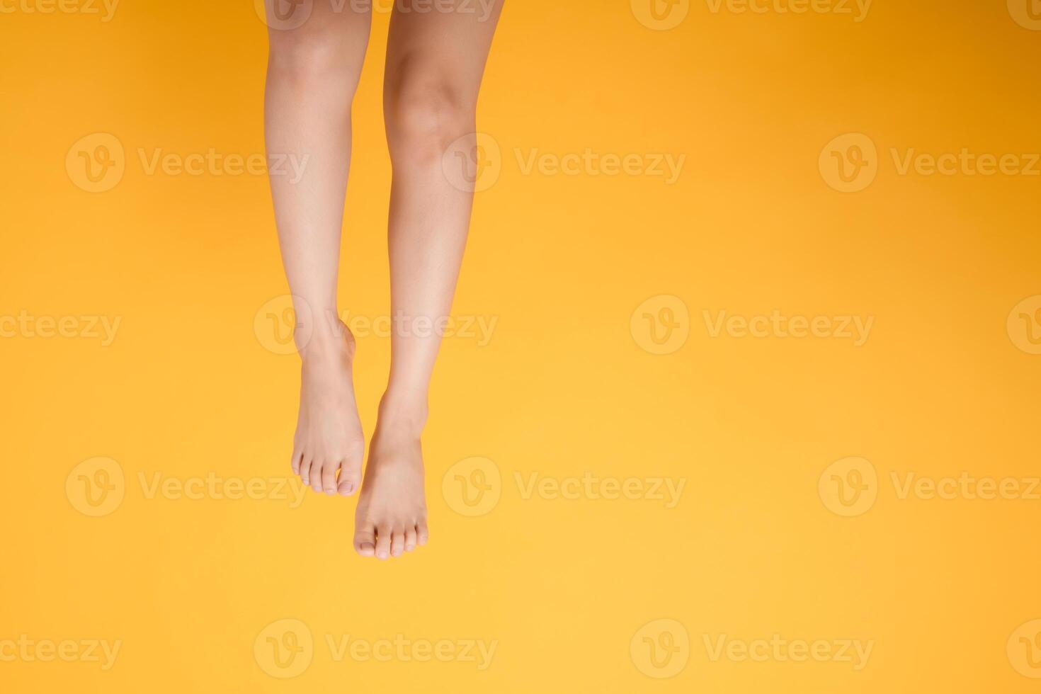 smooth and soft touch with a 30s person's close up legs against vibrant yellow background. Gentle and velvety foot concept. photo