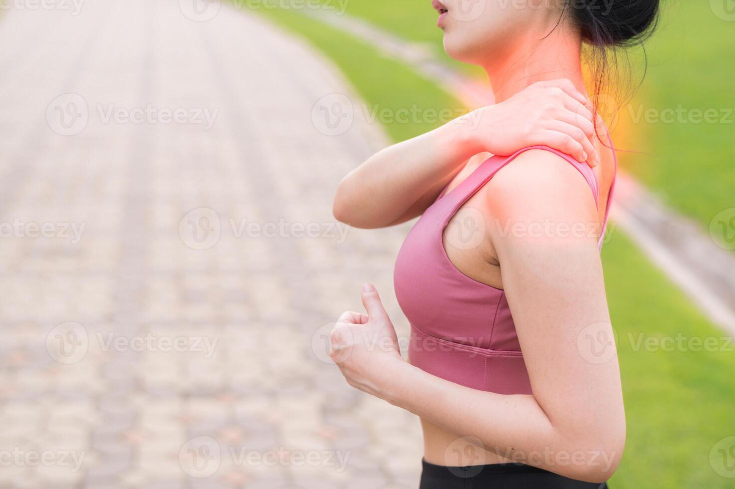 Woman jogger. young 30s asian female wearing pink sportswear holding her back pain after running exercise in public park. Pain in activity concept. photo