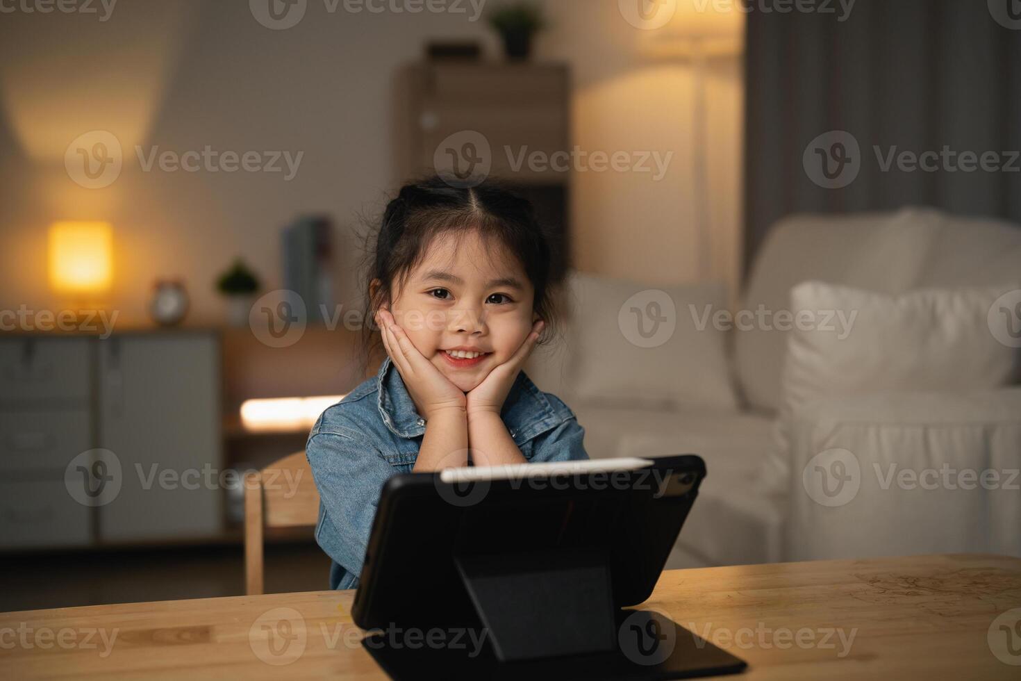 Asian child girl looking using and touch tablet display screen. Baby smiling funny time to use tablet. Too much screen time. Cute girl watching videos while tv, Internet addiction concept. photo