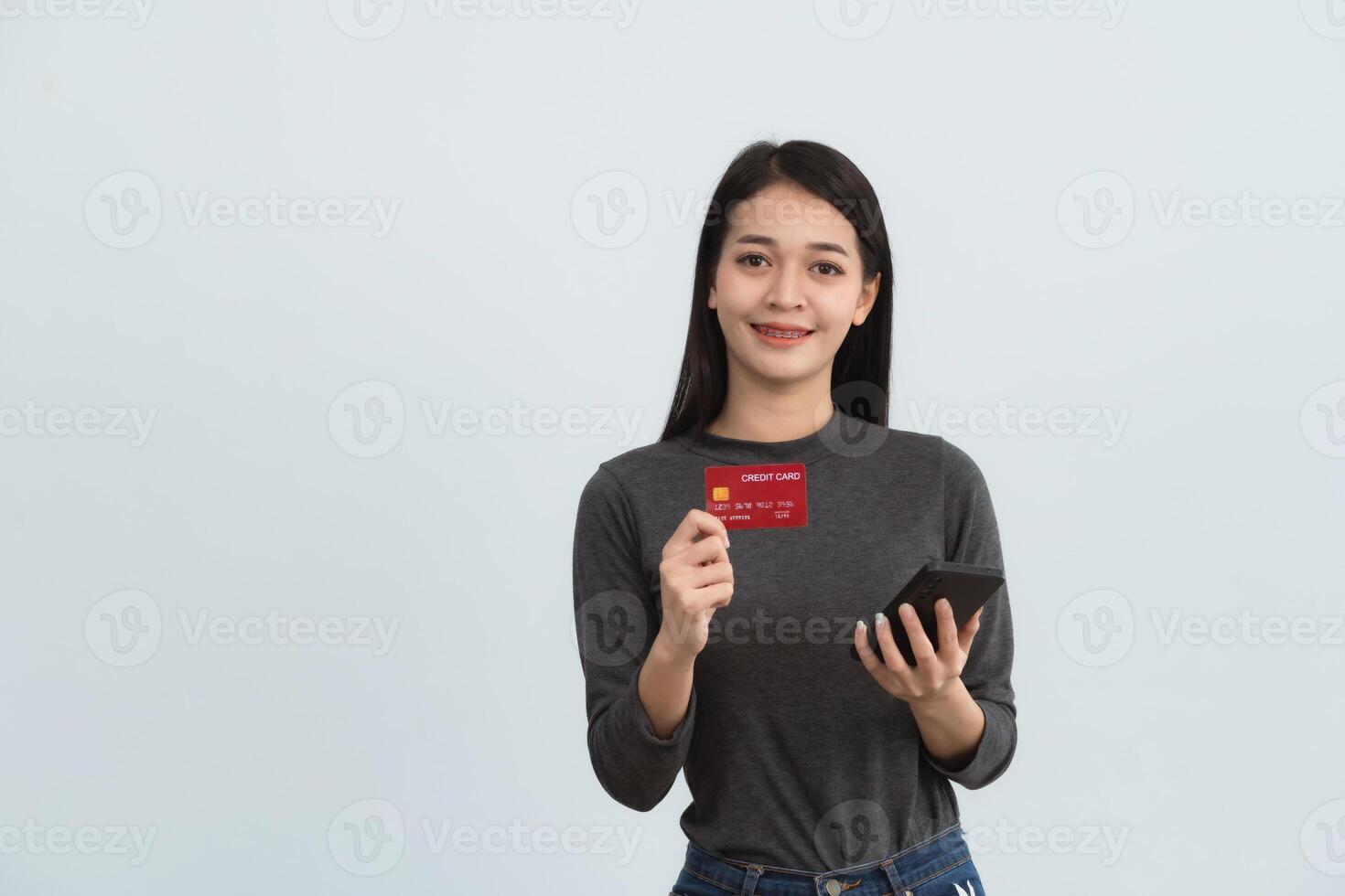 Asian woman holding showing credit card and mobile phone to shopping online isolated on white or gray background studio. Online shopping, e-commerce, internet banking, spending money concept. photo