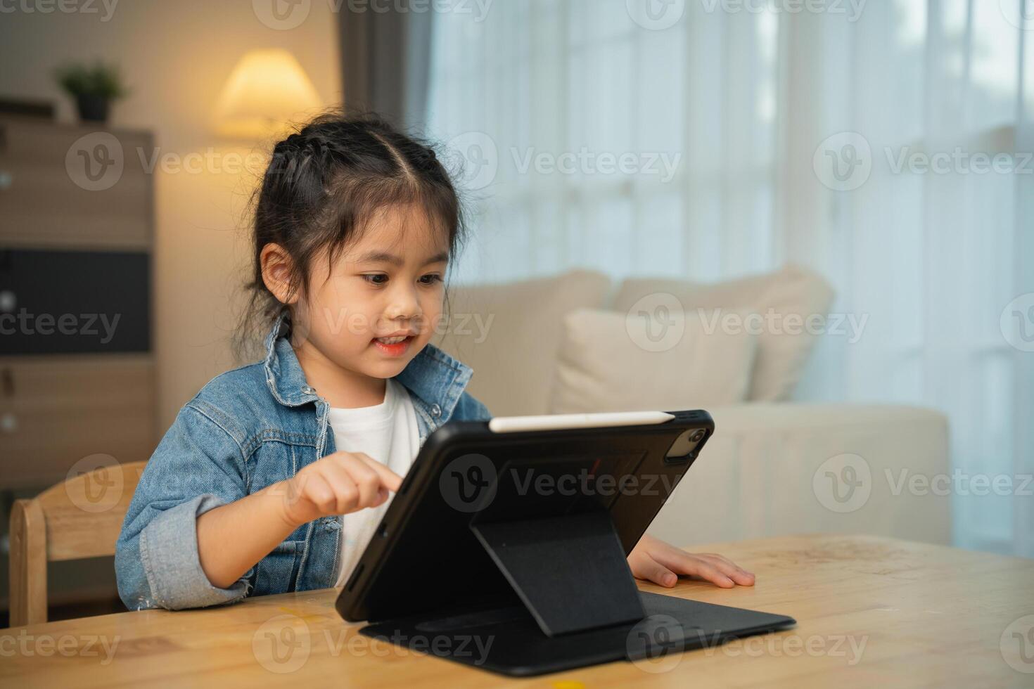 Asian child girl looking using and touch tablet display screen. Baby smiling funny time to use tablet. Too much screen time. Cute girl watching videos while tv, Internet addiction concept. photo