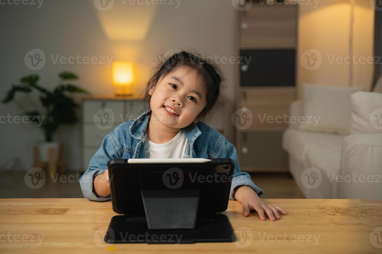 Asian child girl looking using and touch tablet display screen. Baby smiling funny time to use tablet. Too much screen time. Cute girl watching videos while tv, Internet addiction concept. photo
