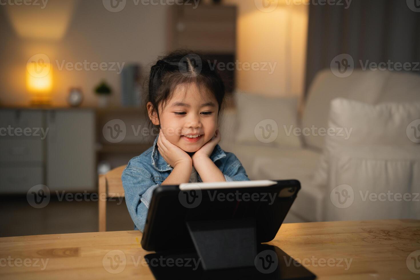 Asian child girl looking using and touch tablet display screen. Baby smiling funny time to use tablet. Too much screen time. Cute girl watching videos while tv, Internet addiction concept. photo