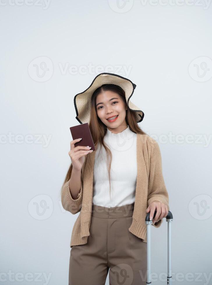 Young Asian tourist woman smiling wearing hat and holding luggage, passport to prepare going to travel on holidays isolated on white or grey studio background. photo