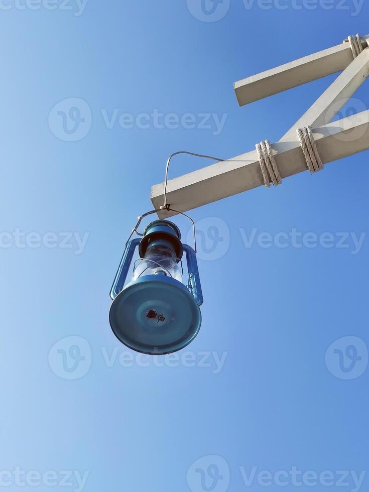 Old fashioned antique blue color oil or gas lamp or lantern hanging off the wooden beam against blue sky, metal retro light vintage lamp, with copy space for business concept photo