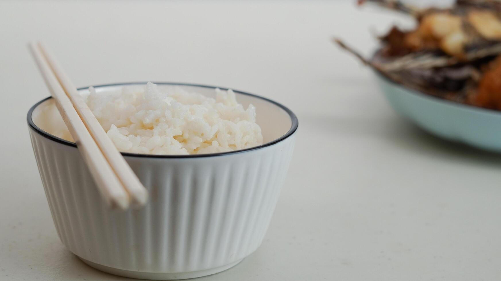 White rice in a bowl and fried fish on a white plate are served on the table photo