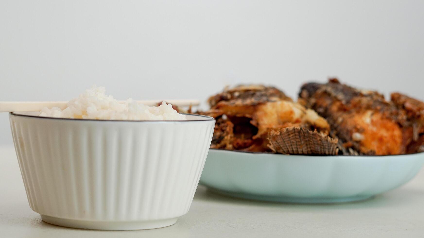 White rice in a bowl and fried fish on a white plate are served on the table photo