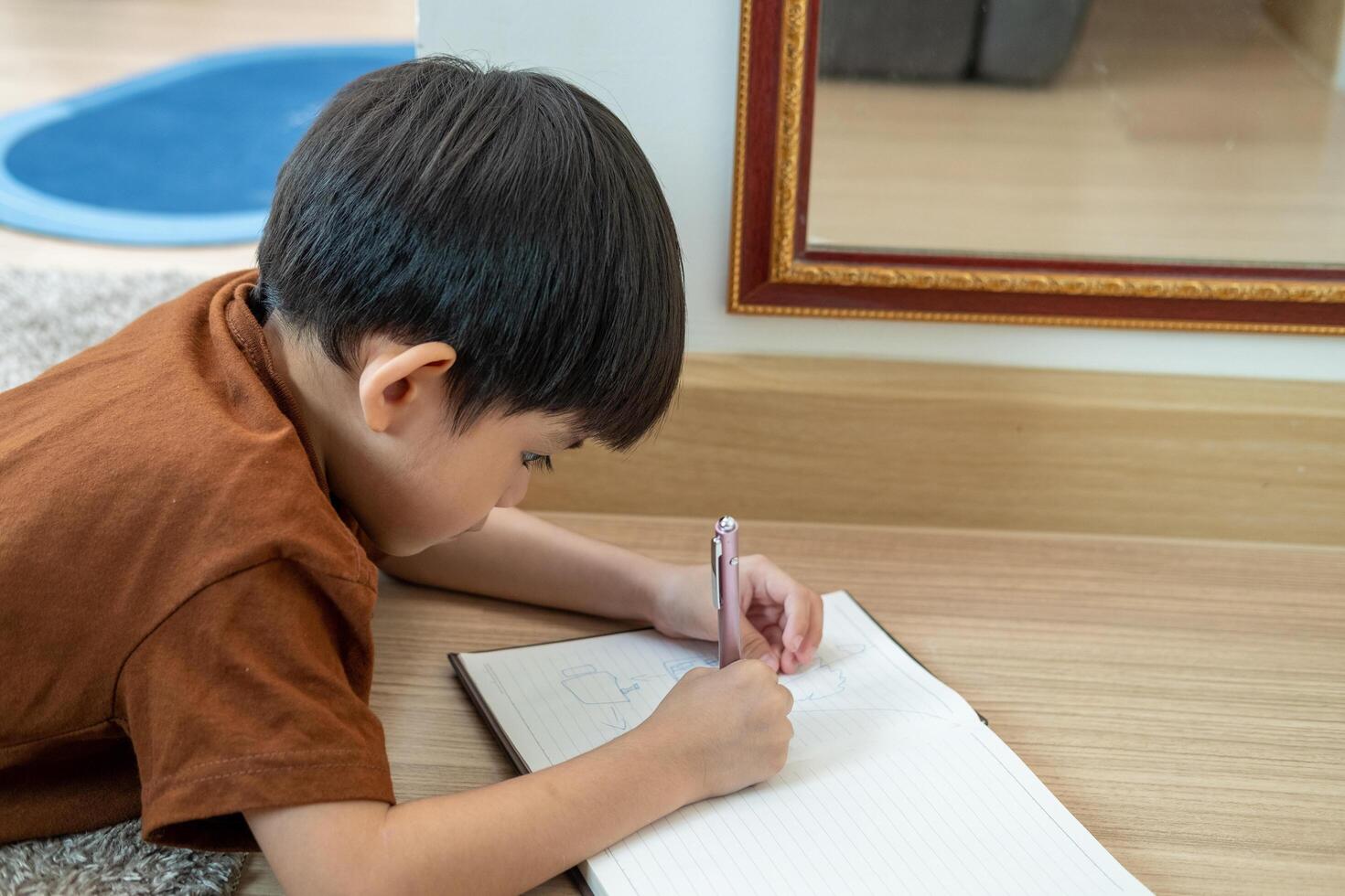 A little Asian boy was lying on the floor drawing on paper. photo